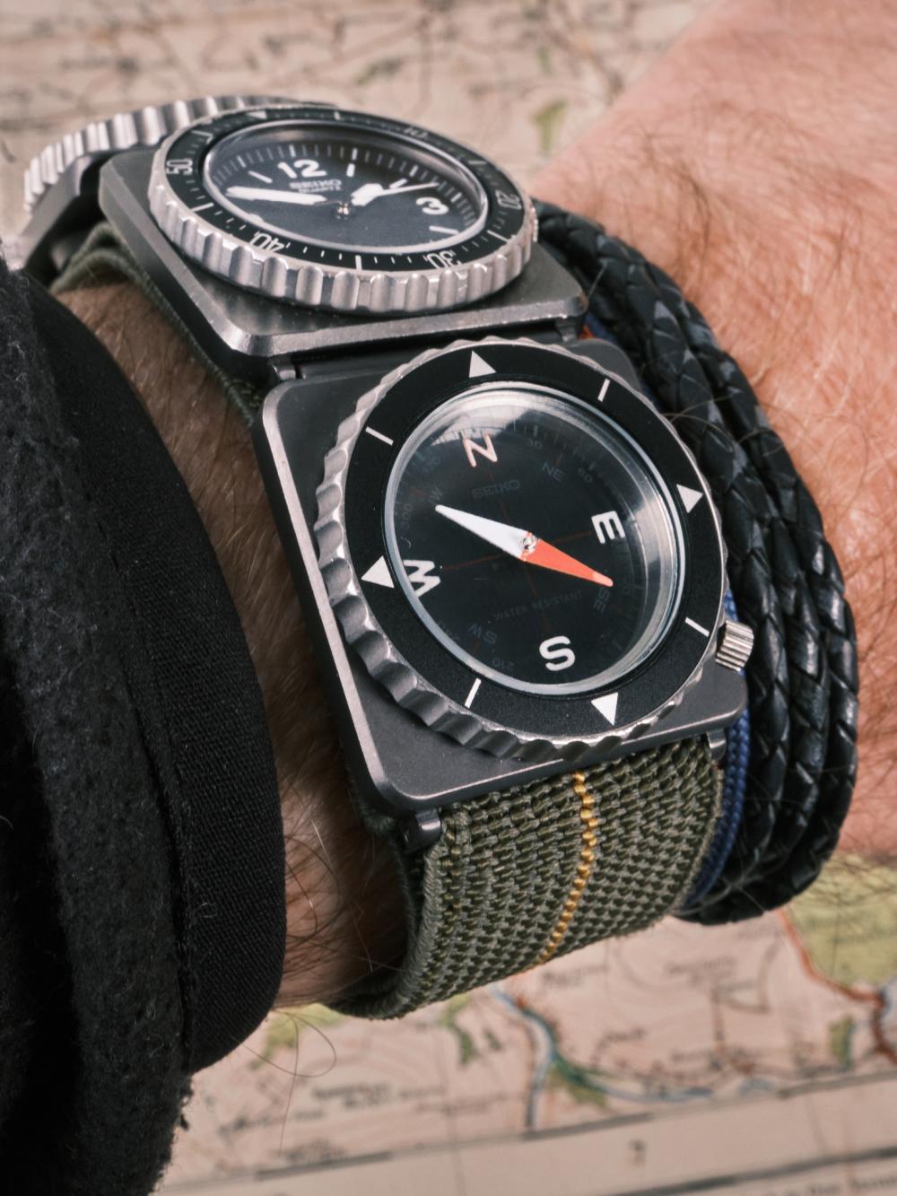 A Seiko Fieldmaster Contra watch worn on the wrist, featuring a black quartz time module with bold Arabic numerals paired with a compass module below, both housed in square black cases on a green fabric strap, photographed against a detailed vintage map background.