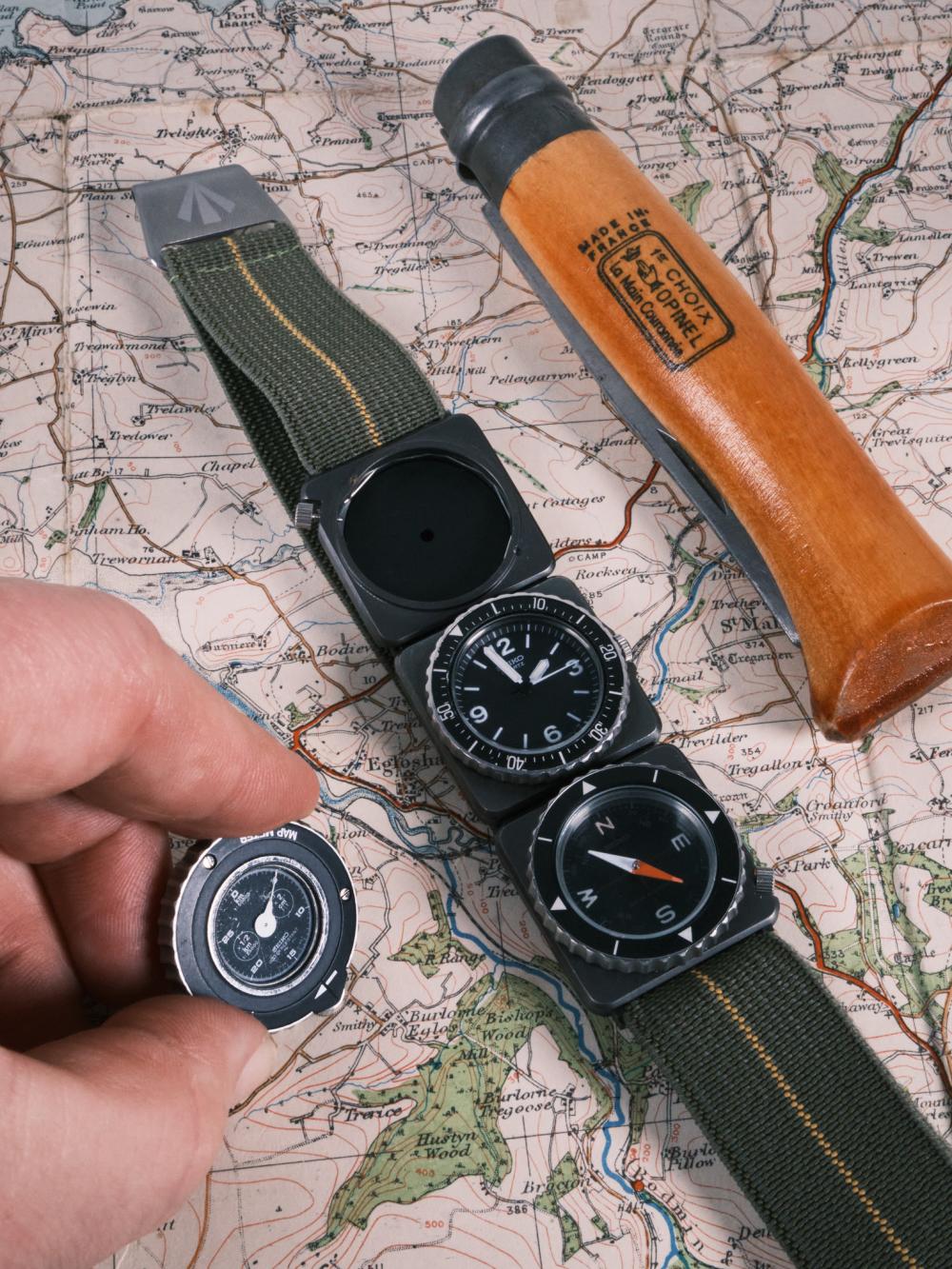 Seiko Fieldmaster Contra modular watch laid across a vintage map, showing the quartz time module and compass module on a green fabric strap, with a hand holding a removable map meter insert beside a wooden-handled knife.