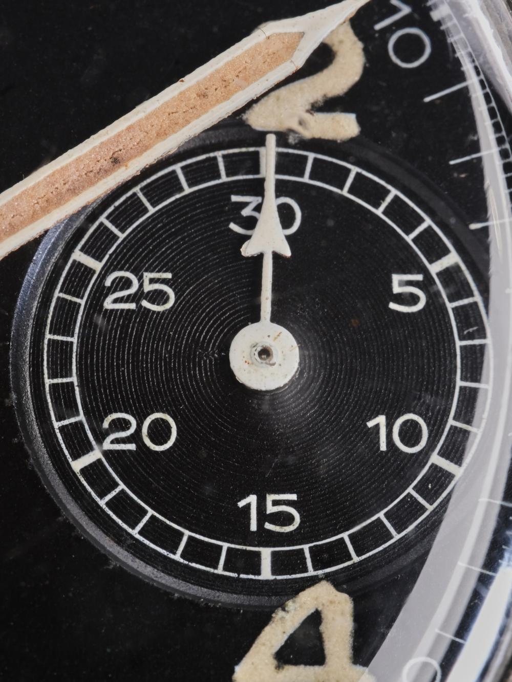 A macro photograph of the right-hand chronograph sub-dial on a vintage Hanhart 417 ES. The image highlights the finely textured black register, crisp white minute scale, aged luminous numeral "2" and the heavily patinated syringe minute hand above. Fine scratches on the acrylic crystal and the warm, aged lume illustrate the watch's decades of honest wear and vintage character.
