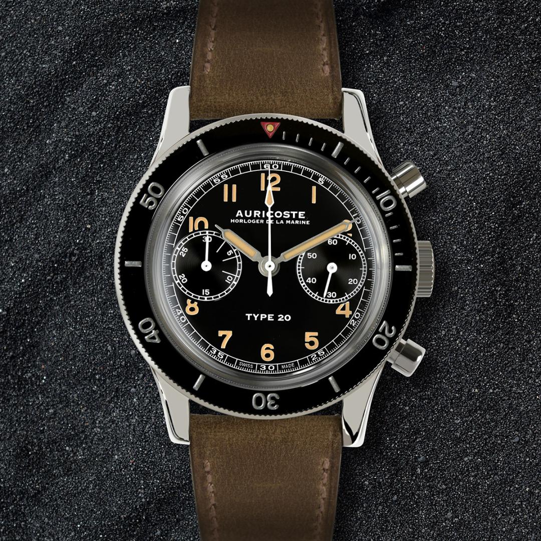 Auricoste Type 20 chronograph with a black bi-compax dial, luminous Arabic numerals and hands, twin chronograph pushers and a black rotating bezel with elapsed-time markings. The stainless steel pilot’s watch is fitted to a brown leather strap, reflecting the functional design language of the French Type 20 military chronograph.